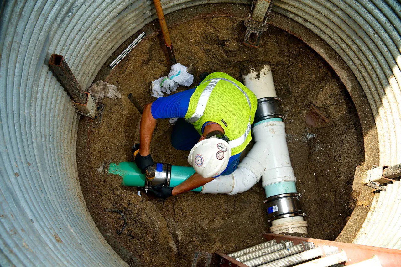 A Bob Frame Plumbing technician working inside a shored excavation